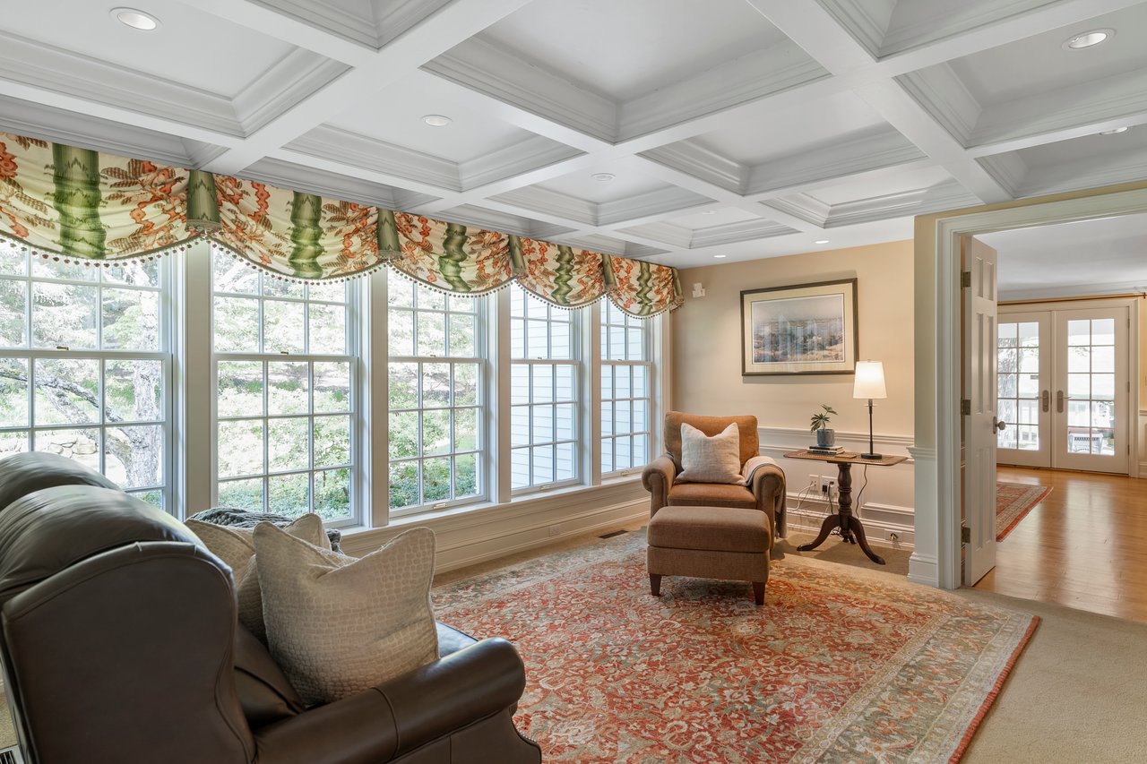 A bank of windows in a cozy study offers a serene retreat with coffered ceiling and built-ins galore