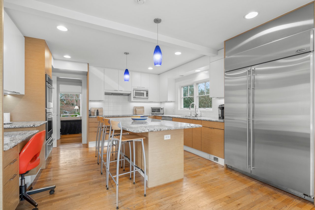 Kitchen with built in appliances, light wood-style flooring, backsplash, and a kitchen breakfast bar