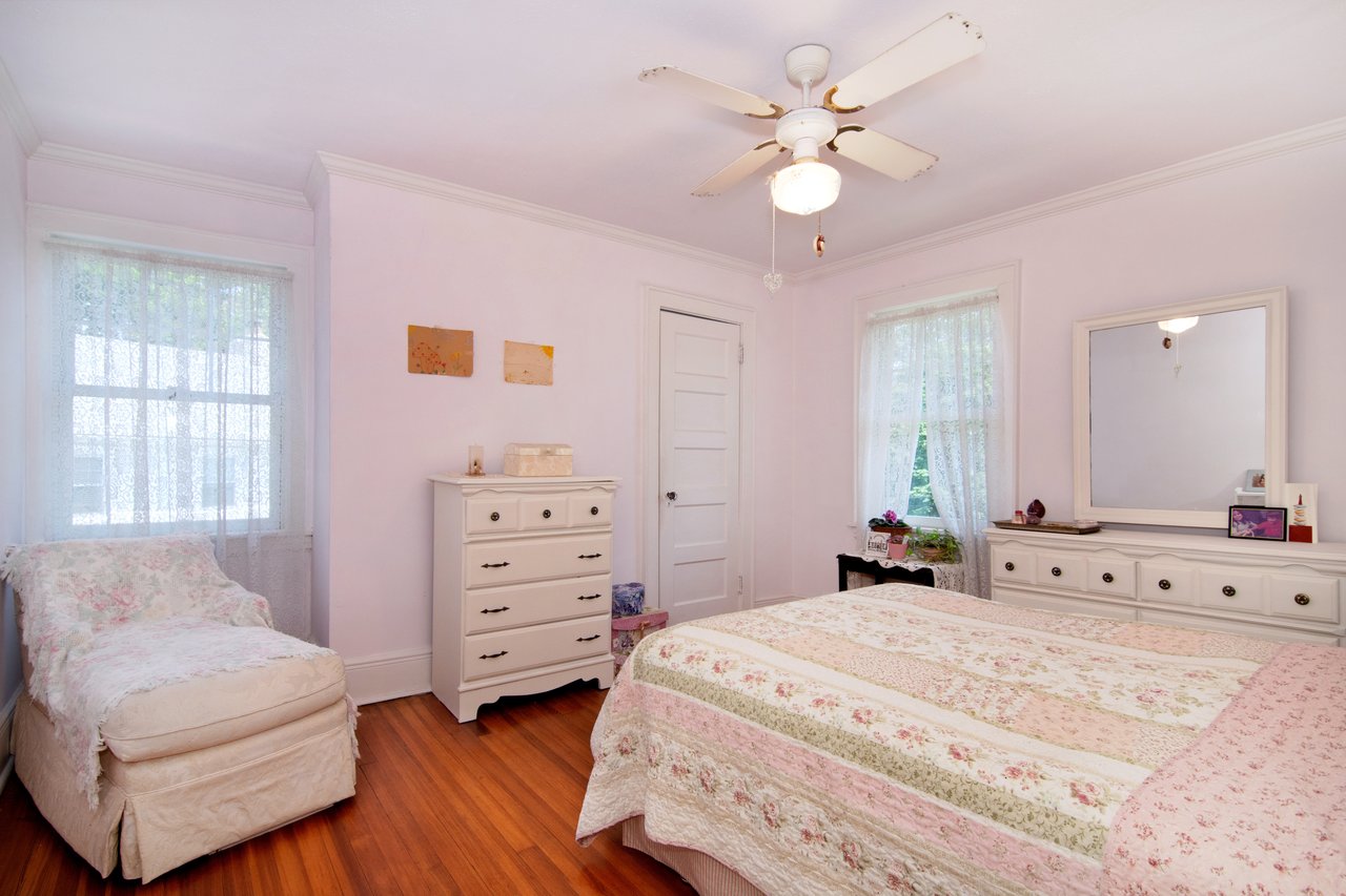 A warm and inviting bedroom features hardwood floors, a ceiling fan for year-round comfort, and plenty of natural light....