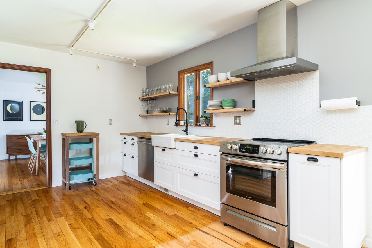 Kitchen with butcher block countertops, appliances with stainless steel finishes, wall chimney range hood, and open shelves