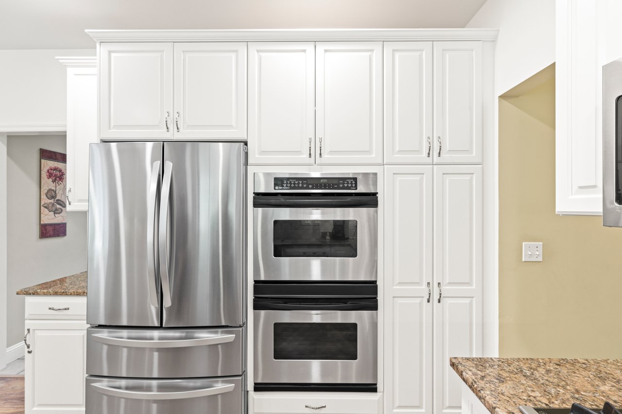 Kitchen with appliances with stainless steel finishes, light stone countertops, and white cabinets