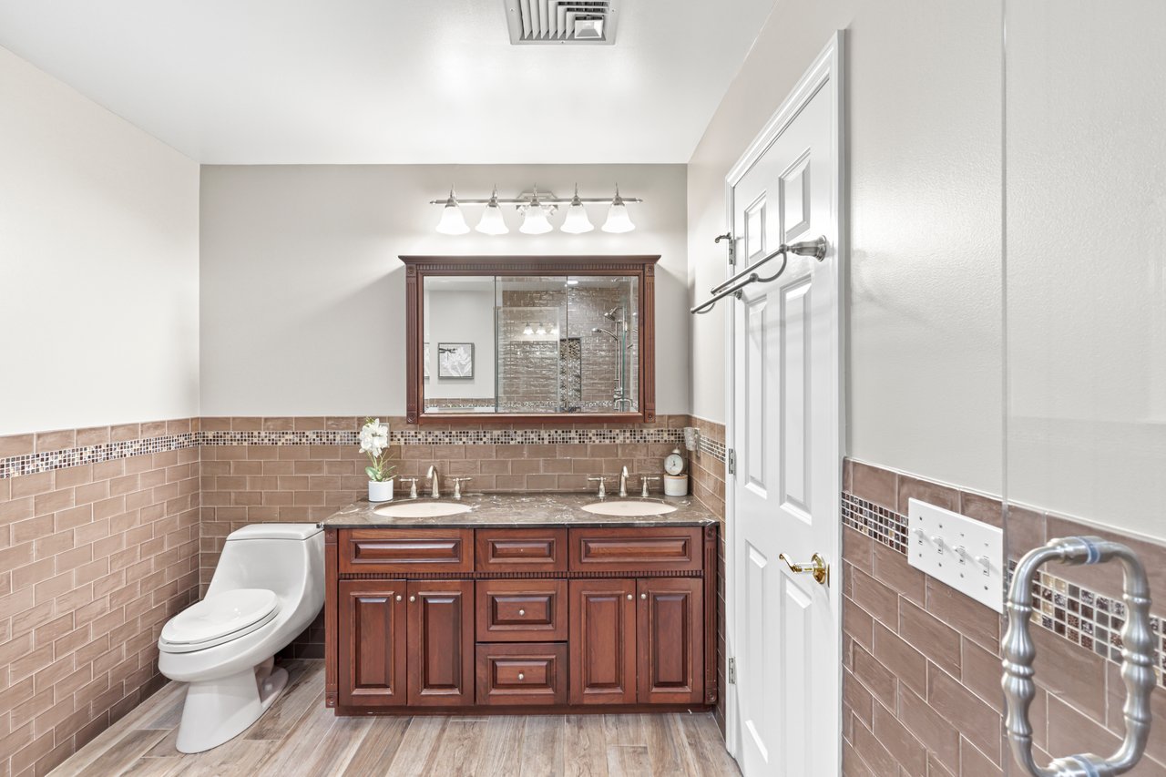 Primary Bathroom with tile walls, wainscoting, double vanity, tiled shower, and wood finished floors