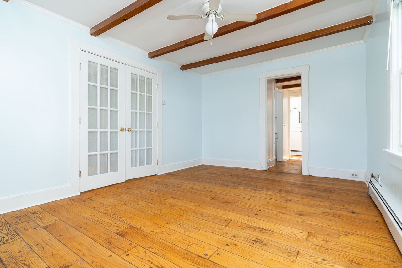 Spare room with french doors, a baseboard radiator, beamed ceiling, ceiling fan, and light wood-type flooring