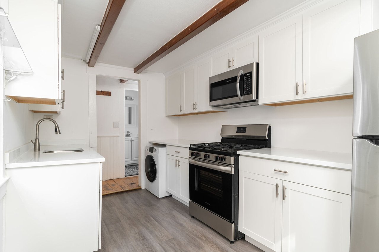 Kitchen featuring stainless steel appliances, beam ceiling, light wood finished floors, light countertops, and white cabinetry
