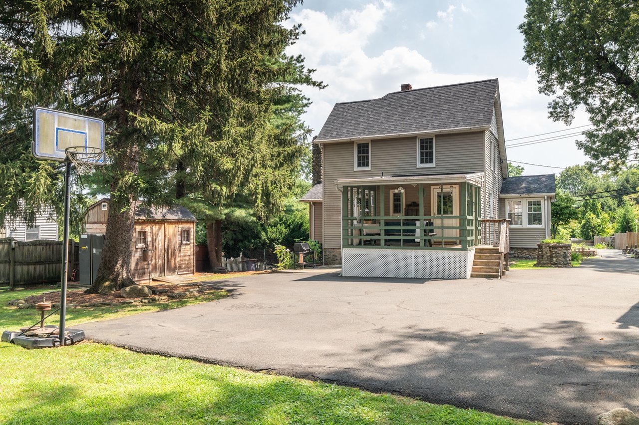 Rear view of property with a porch, roof with shingles, a chimney, and a storage unit