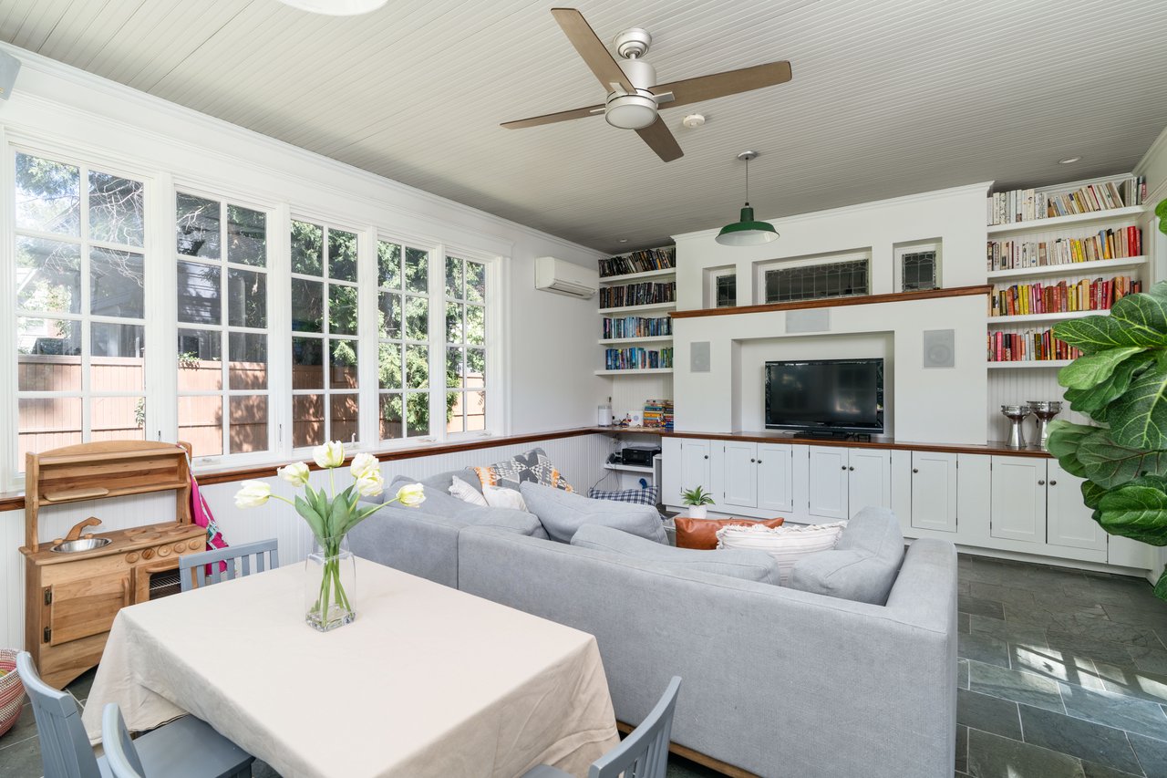 Living room with a ceiling fan, dark stone finish flooring, a wall mounted AC, ornamental molding, and built in shelves