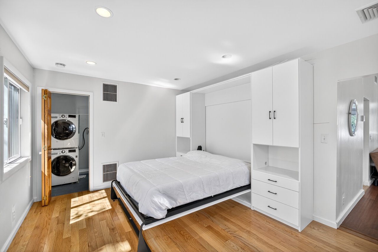 Primary Bedroom with Murphy bed or can be closed and used as a wall, stackable washer and clothes dryer in separate laundry room as seen light wood-type flooring, and recessed lighting