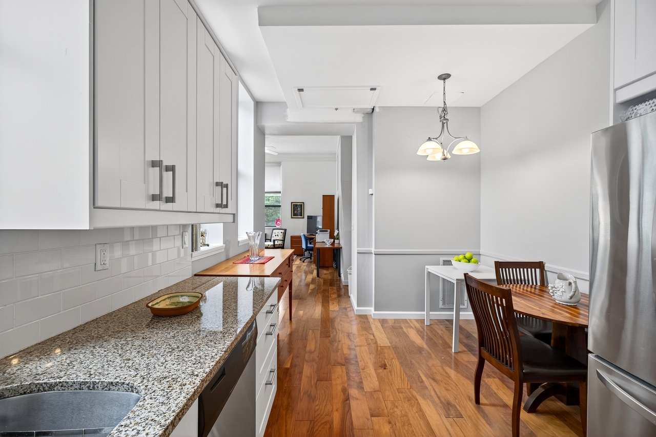Kitchen with white cabinetry, light stone counters, light wood-type flooring, stainless steel appliances, and decorative light fixtures...