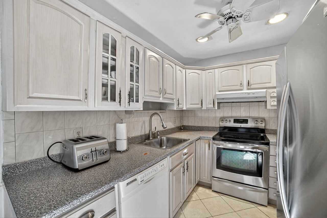 Kitchen with appliances with stainless steel finishes, under cabinet range hood, light tile patterned floors, glass insert cabinets, and tasteful backsplash