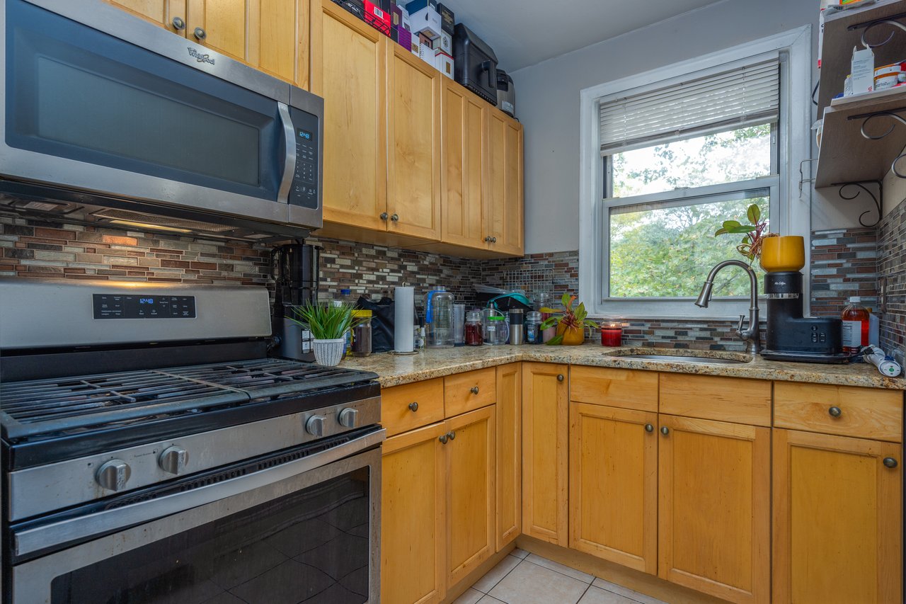 Kitchen featuring stainless steel appliances, decorative backsplash, light tile patterned floors, light stone countertops, and brown cabinets