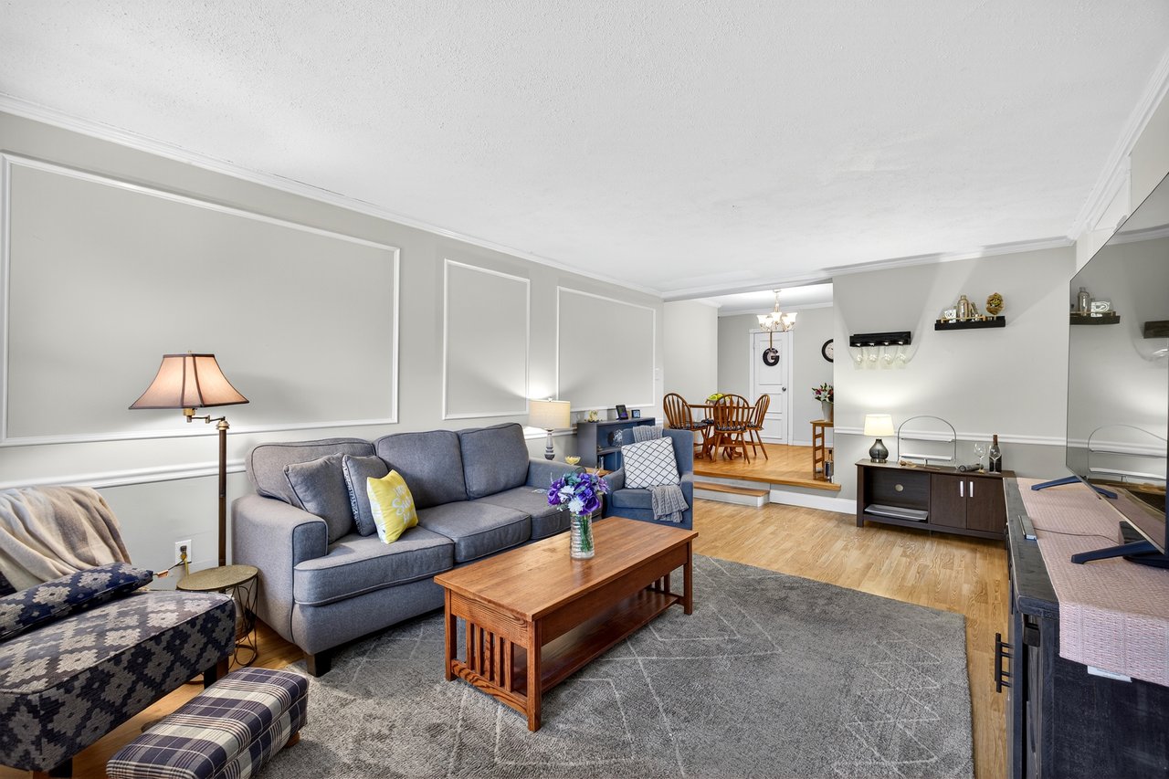 Living area featuring wood finished floors, crown molding, a chandelier, and a decorative wall