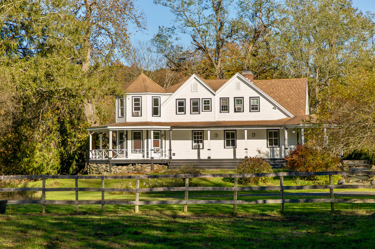 View of front of house with a porch, a chimney, roof with shingles, and view of wooded area