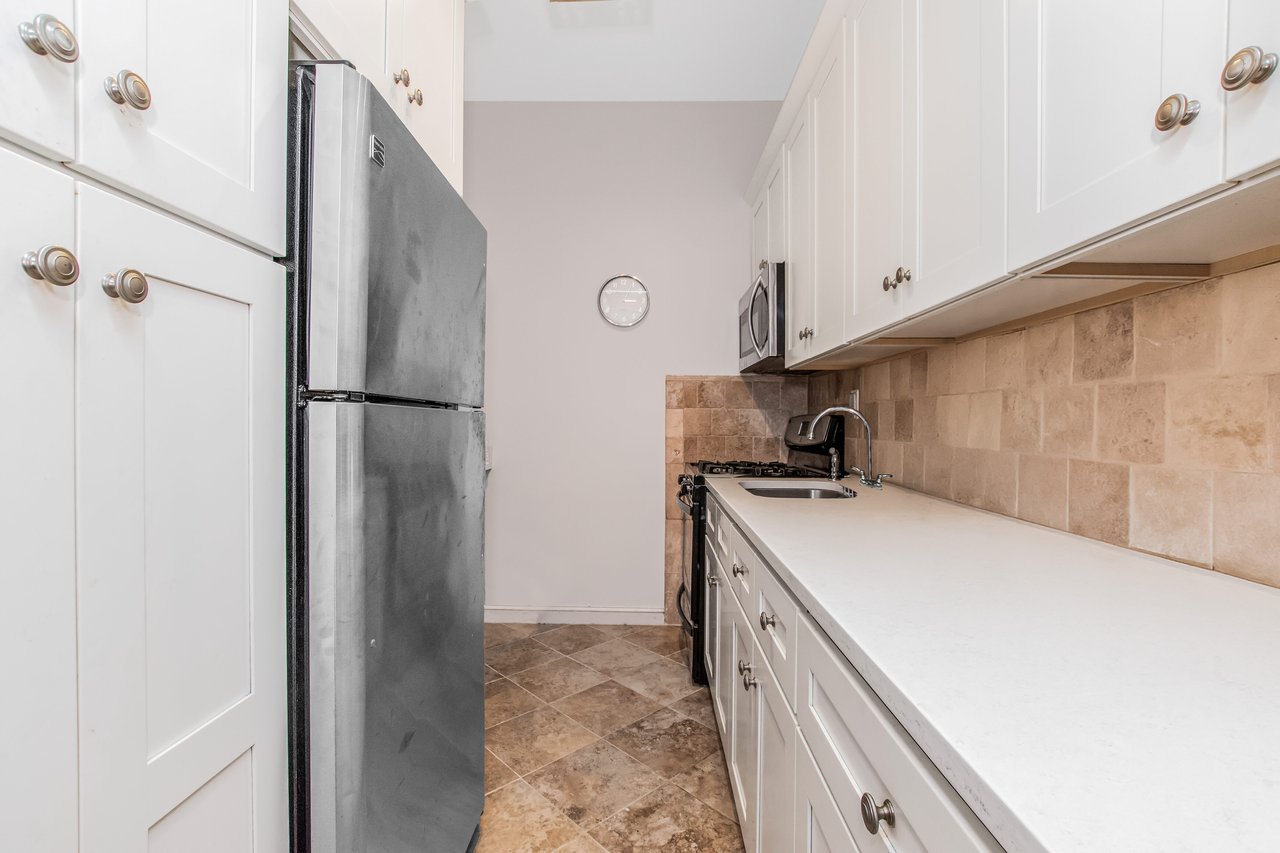 Kitchen with stainless steel appliances, white cabinetry, backsplash, and light stone countertops