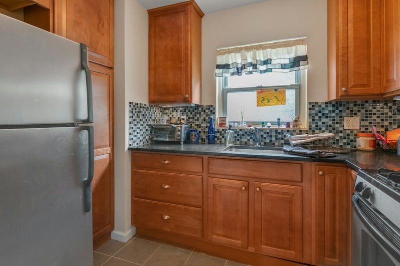 Kitchen with freestanding refrigerator, dark countertops, brown cabinets, and tasteful backsplash