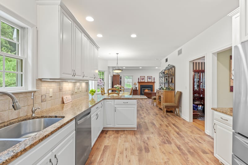 Kitchen featuring stainless steel appliances, light wood-style flooring, a warm lit fireplace, a peninsula, and white cabinets