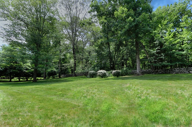 View of rear grounds with mature trees and beautiful stone wall.