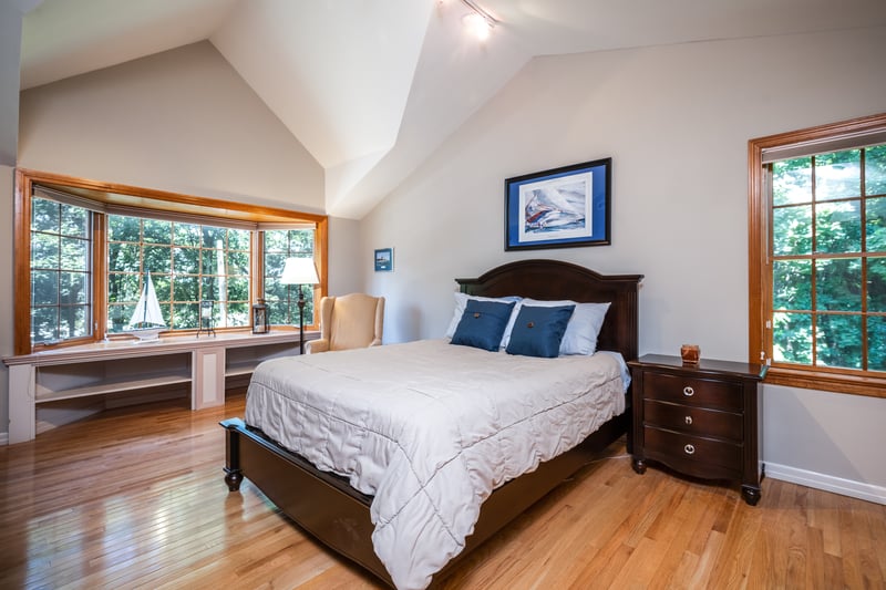 Primary Bedroom with vaulted ceiling, hardwood floors, and multiple windows with views of nature.