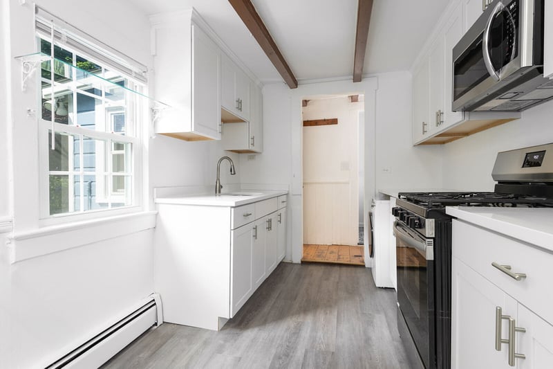 Kitchen with appliances with stainless steel finishes, light wood-style flooring, a baseboard heating unit, beamed ceiling, and light countertops