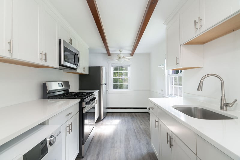 Kitchen with appliances with stainless steel finishes, beam ceiling, light countertops, white cabinets, and wood finished floors