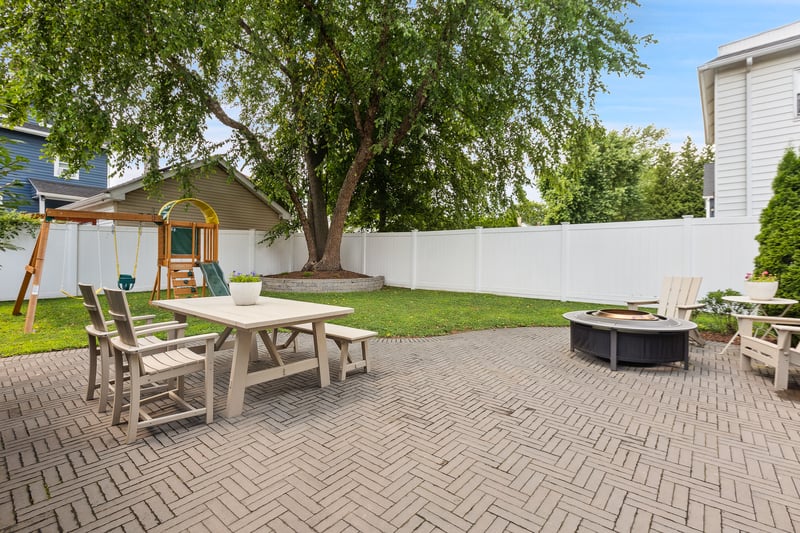 Fenced backyard with a patio, a playground, an outdoor fire pit, and outdoor dining space...