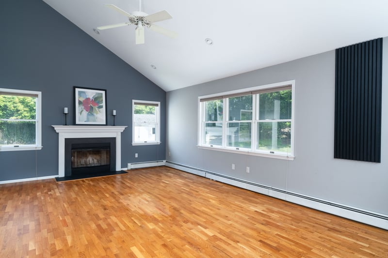 Unfurnished living room with wood finished floors, high vaulted ceiling, a glass covered fireplace, a baseboard radiator, and a ceiling fan