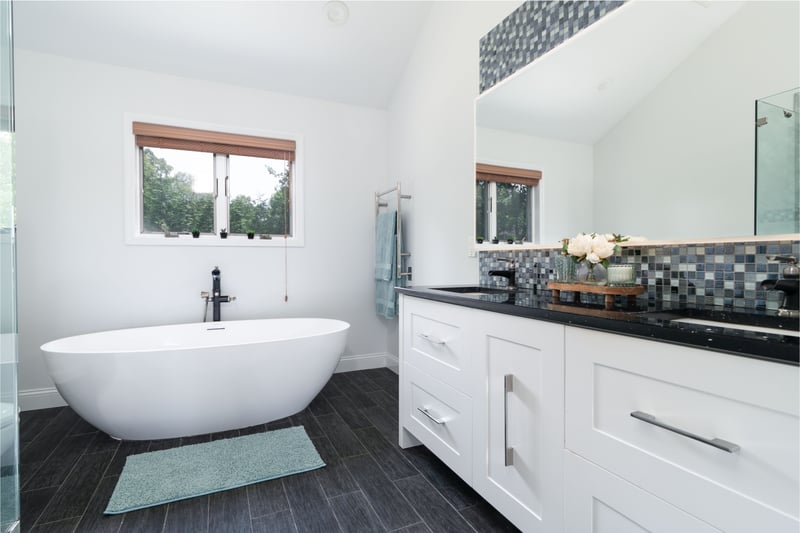Full bathroom featuring lofted ceiling, double vanity, decorative backsplash, a freestanding tub, and wood finish floors