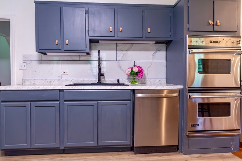 Kitchen with tasteful backsplash, stainless steel appliances, blue cabinetry, and light wood-type flooring