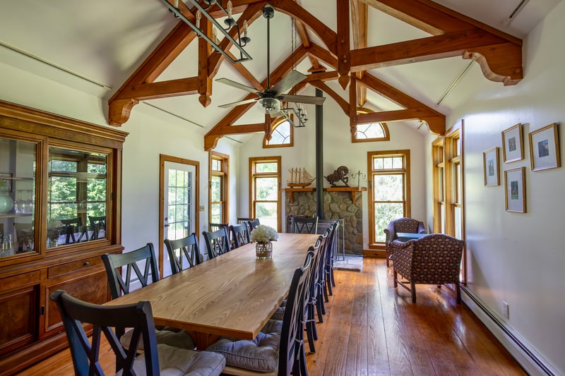 Dining space with baseboard heating, hardwood / wood-style flooring, a wood stove, ceiling fan, and beam ceiling