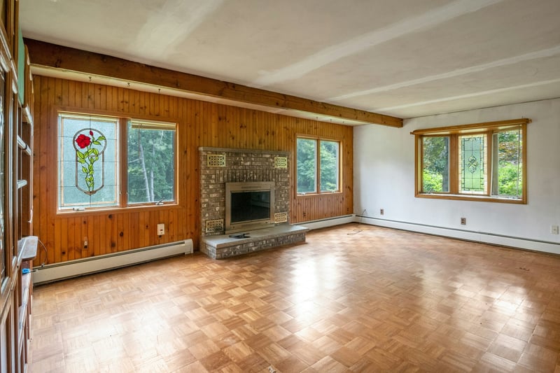 Unfurnished living room with a baseboard heating unit, beam ceiling, wood walls, and a fireplace...
