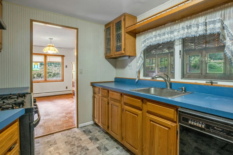 Kitchen featuring black appliances, brown cabinetry, wallpapered walls, a baseboard radiator, and glass insert cabinets...