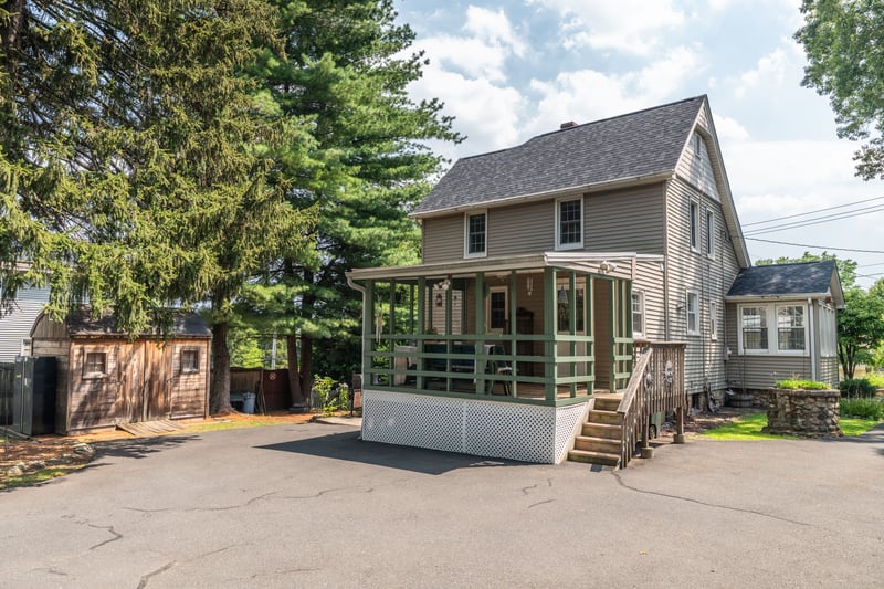 View of front of home featuring roof with shingles, covered porch, a shed, and asphalt driveway