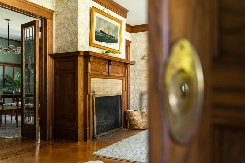 Detailed view of a fireplace with flush hearth, wallpapered walls, wood finished floors, a chandelier, and ornamental molding