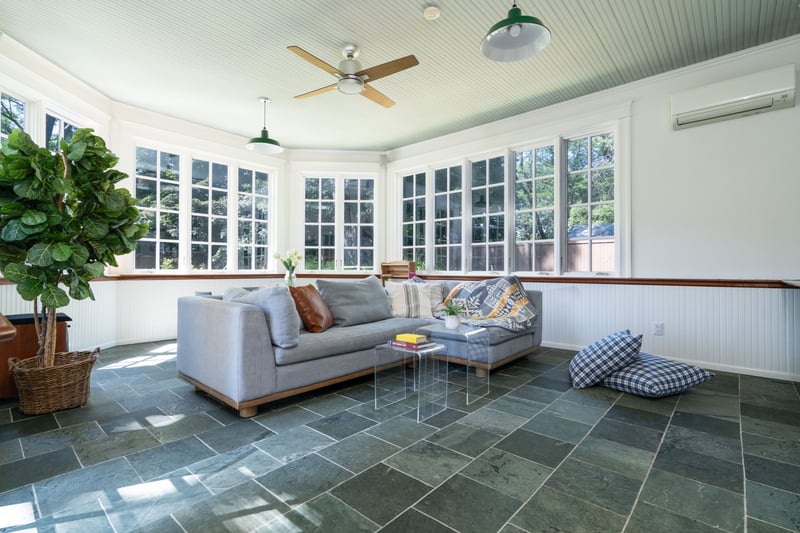 Sunroom / solarium featuring stone tile floors, a wall unit AC, and wainscoting
