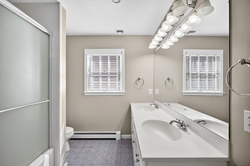 Full hall Bathroom featuring double vanity, plenty of natural light, and shower / bath combination with glass door.