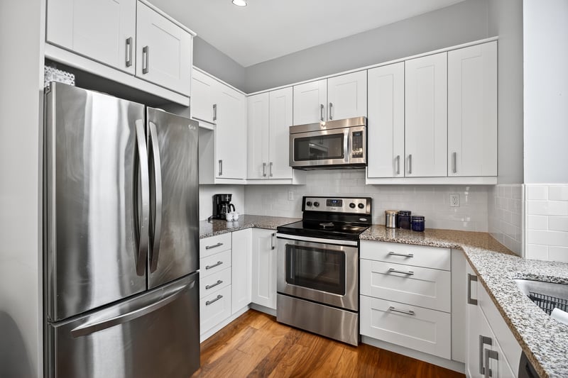 Large Updated Kitchen featuring stainless steel appliances, white cabinets, light stone counters, and dark wood-type flooring...