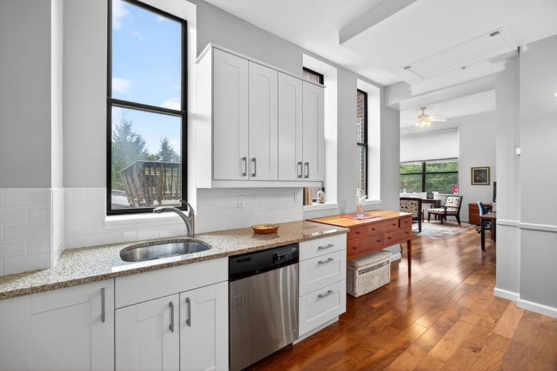 Kitchen with stainless steel dishwasher, dark wood-style floors, light stone countertops, decorative backsplash, and white cabinets...
