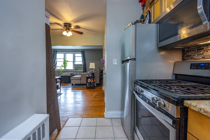 Kitchen with stainless steel appliances, light tile patterned flooring, a ceiling fan, decorative backsplash, and light stone counters