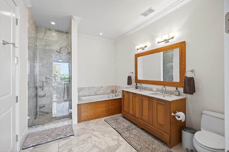 Bathroom featuring a bath, a marble finish shower, light marble finish floors, double vanity, and crown molding...