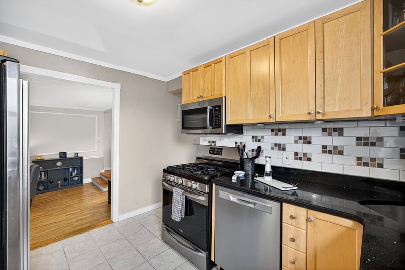 Kitchen with appliances with stainless steel finishes, tasteful backsplash, light tile patterned floors, light brown cabinets, and ornamental molding