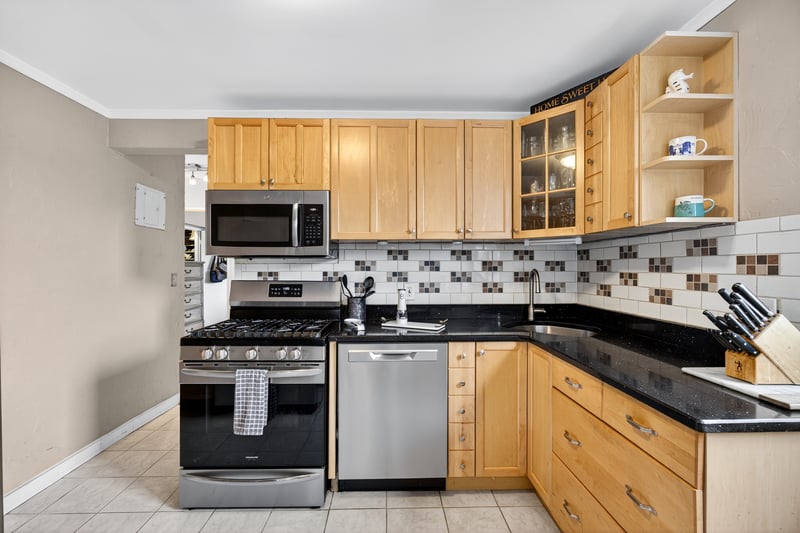 Kitchen featuring stainless steel appliances, backsplash, glass insert cabinets, dark stone counters, and open shelves