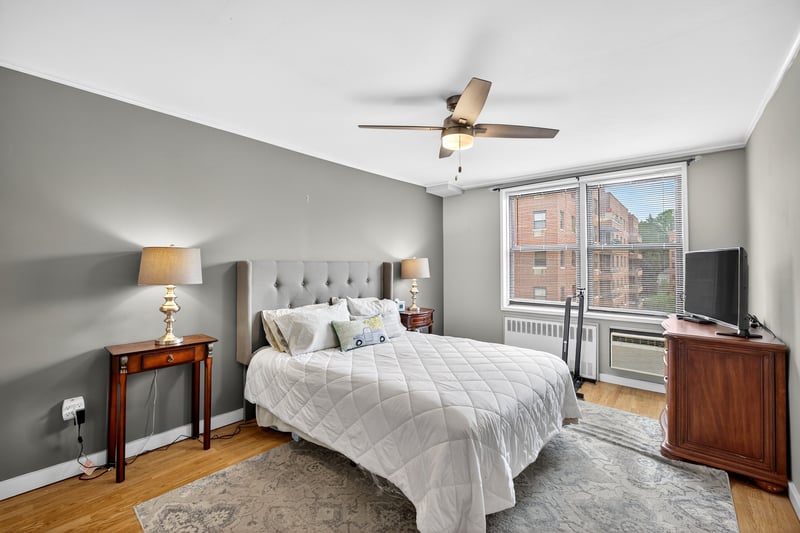 Primary Bedroom with light wood-type flooring, radiator heating unit, a ceiling fan, and a wall unit AC