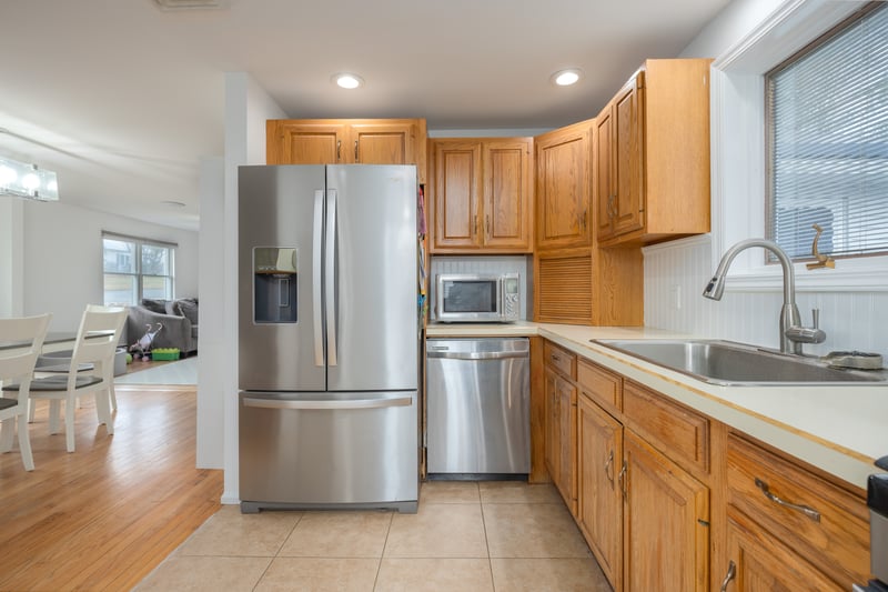 Kitchen with stainless steel appliances, light countertops, light tile patterned floors, brown cabinetry, and decorative backsplash