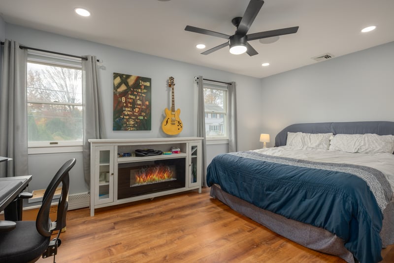 Bedroom with wood finished floors, recessed lighting, a ceiling fan, a glass covered fireplace, and a baseboard heating unit