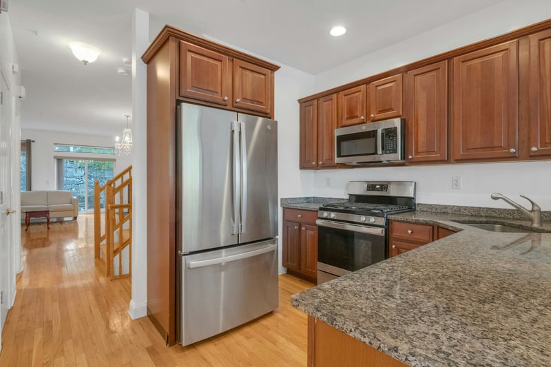 Kitchen with stainless steel appliances, dark stone countertops, brown cabinetry, light wood finished floors, and recessed lighting