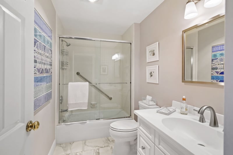 Full bath in the hall with marble floor, Corian topped vanity and tub/shower combination.