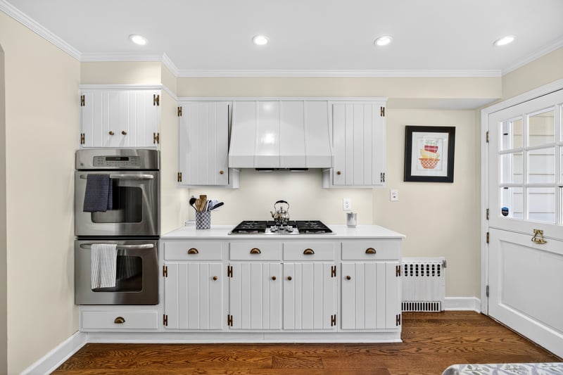Kitchen with white cabinetry, stainless steel appliances, crown molding, radiator heating unit, and dark wood-style floors