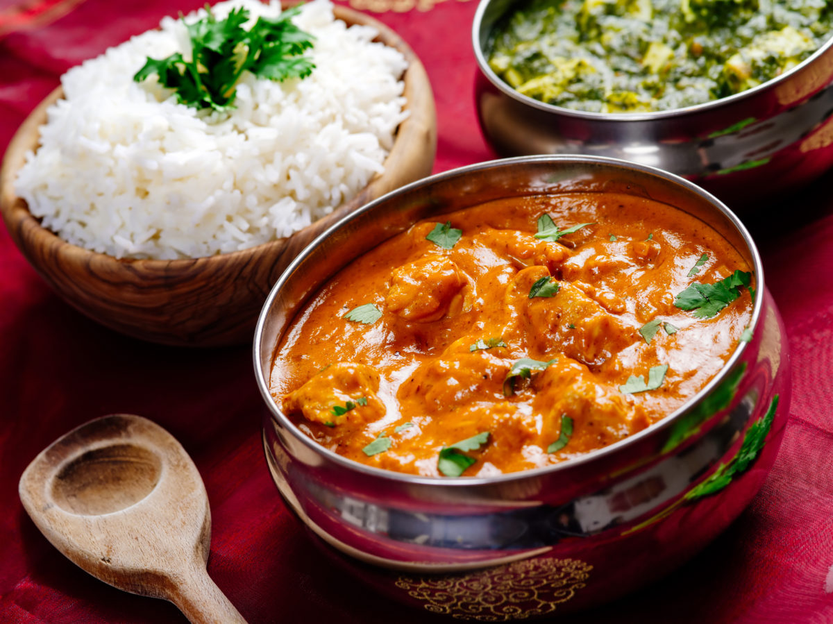 Photo of an Indian meal of Butter Chicken, rice and Saag Paneer. Focus across the Butter Chicken bowl.