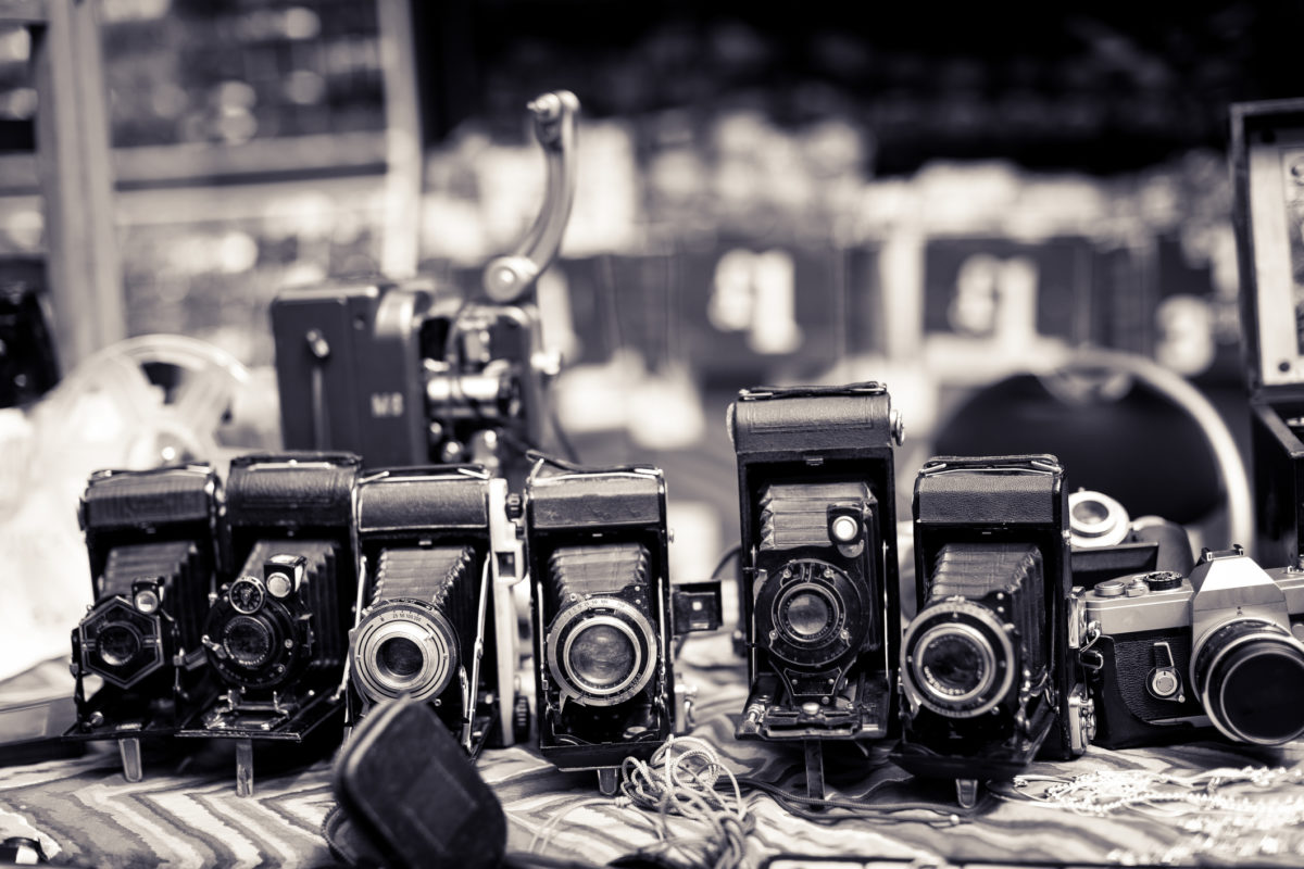 Close up toned monochrome image depicting a display of retro vintage cameras in a row and for sale at an outdoors street market in Notting Hill, London, UK. Focus is on the cameras while the street is defocused in the background. Room for copy space.