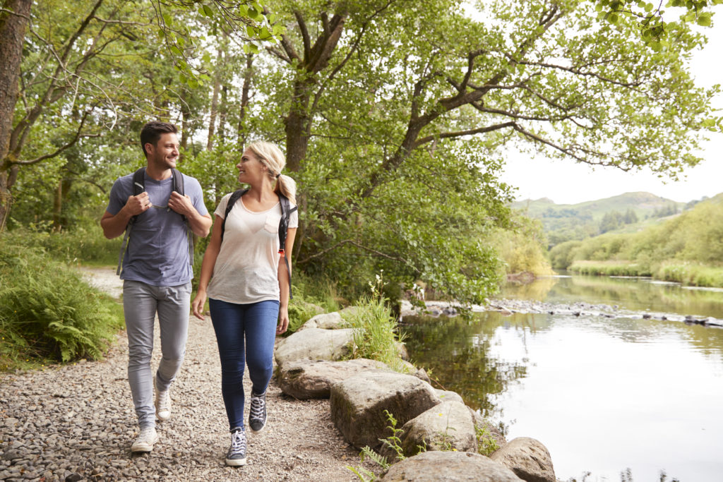 Couple Hiking Along Path By River In UK Lake District